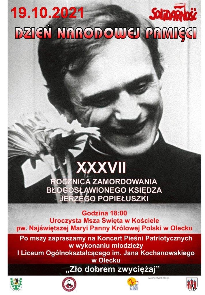 Plakat informacyjny Dnia Narodowej Pamięci Plakat: zdjęcie księdza Jerzego Popiełuszki, z napisem 19.10.2021 r. Dzień Narodowej Pamięci, Solidarność, XXXVII rocznica zamordowania błogosławionego księdza Jerzego Popiełuszki; w kościele Najświętszej Maryi Panny Królowej Polski w Olecku o godz. 18:00 uroczysta msza św., po mszy koncert pieśni patriotycznych