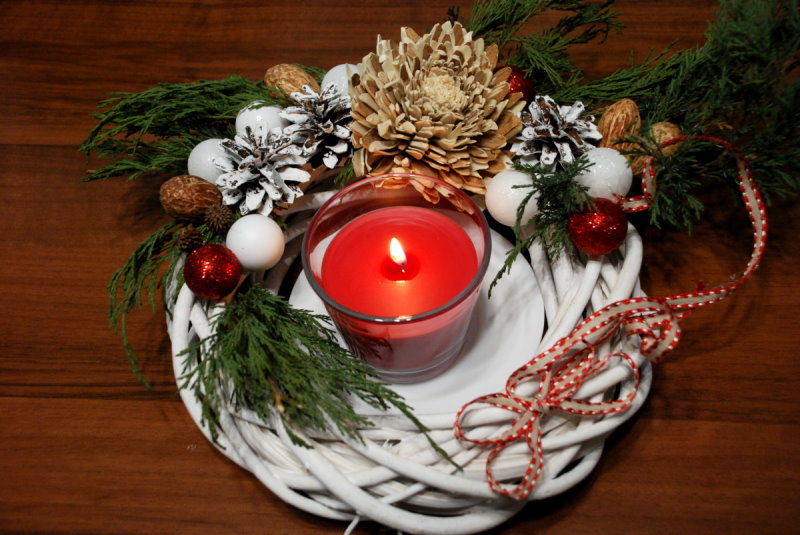 Stroik świąteczny, który składa się między innymi z bombek, szyszek i innych roślin. W środku niego jest zapalona świeczka.