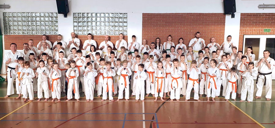 Wspólne zdjęcie kilkudziesięciu karateków. Stoją oni obok siebie w sali. Są ubrani w kimono. Są w wieku od 5 do 65 lat.