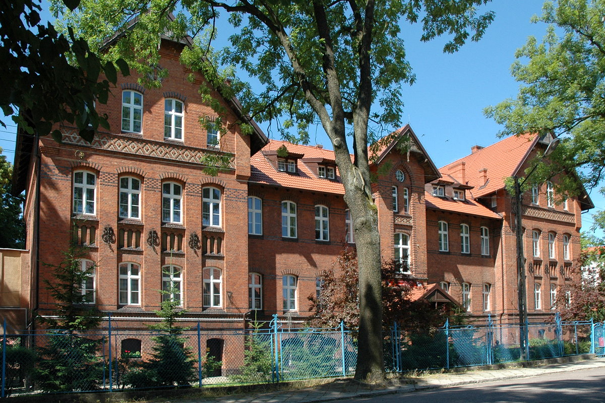 Budynki. Przy nich rośliny, drzewa i ogrodzenie.